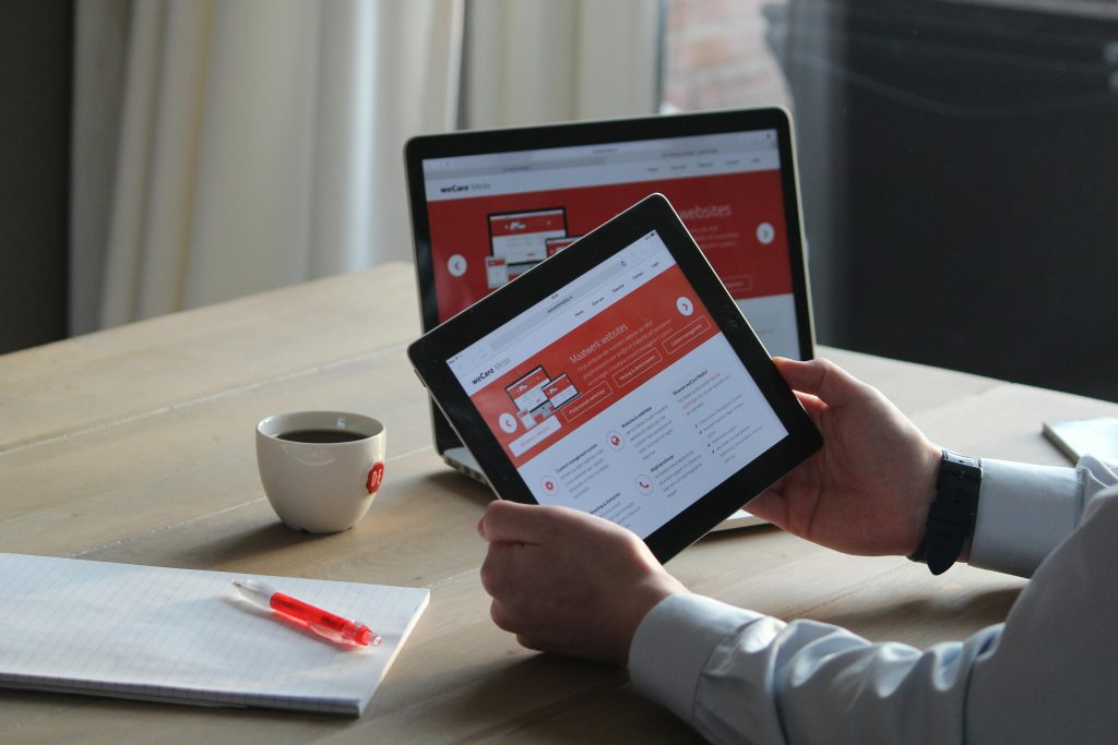 Business professional using a tablet and laptop with a hot drink, focusing on digital content review.